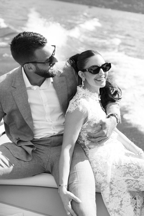 The groom holds the smiling bride as they sit together on a boat on Lake Como.