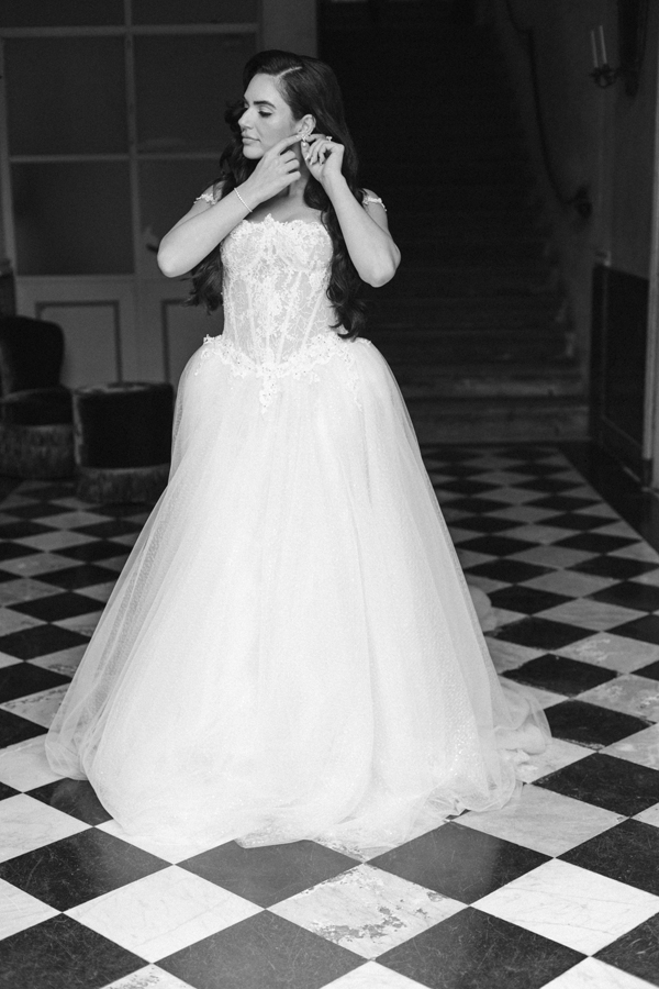 The bride fastens an earring while standing in her wedding dress at Villa Pizzo.