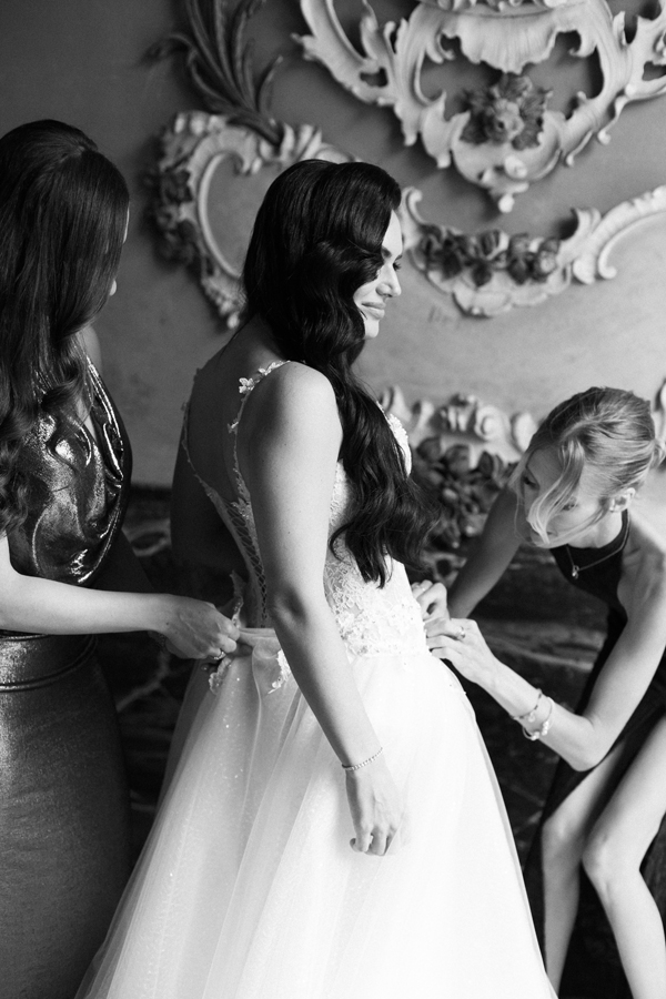 Two women help fasten the bride's wedding dress at Villa Pizzo.