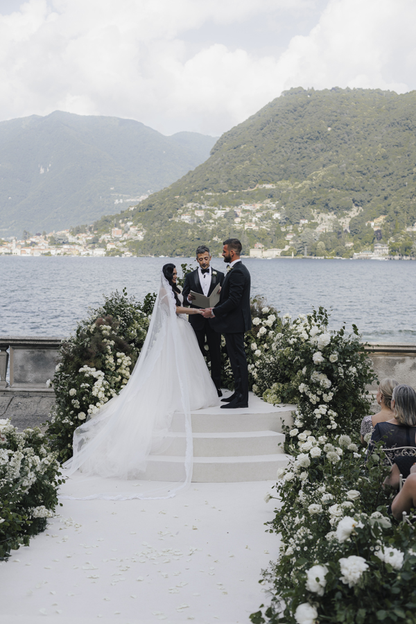 The couple stand together at their flower-lined ceremony beside Lake Como at Villa Pizzo.