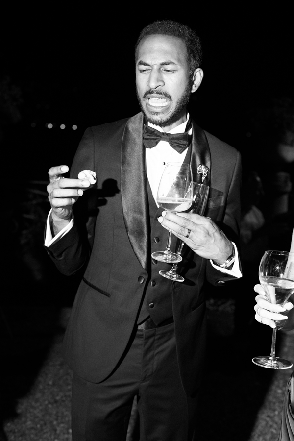 A guest in a tuxedo holds a drink and a bite to eat during the evening celebration.