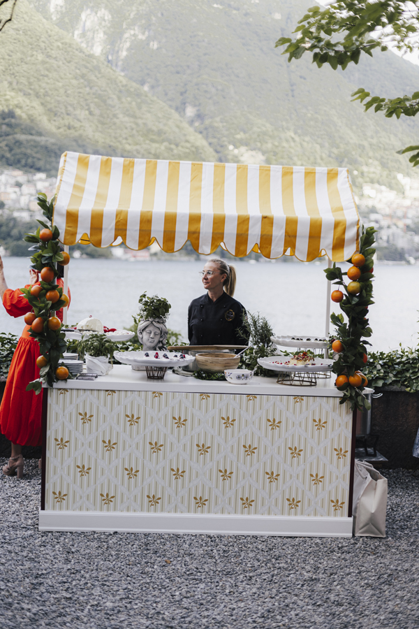 A chef stands behind the striped food cart beside the lake at Villa Regina Teodolinda.