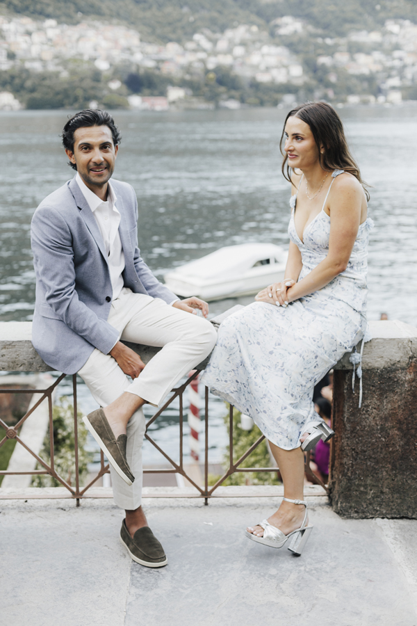 The couple sit together on a low wall overlooking Lake Como.