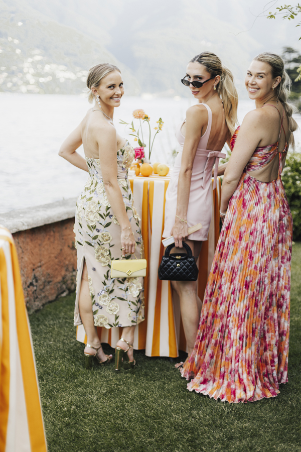Three women talk beside an orange-striped table overlooking Lake Como.