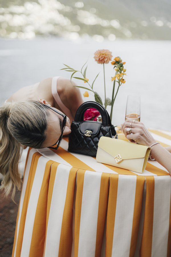 A guest rests her head beside flowers and a drink at a striped table overlooking Lake Como.