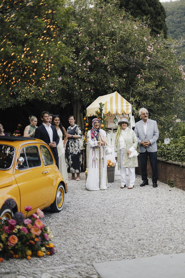 Guests walk through the garden past the yellow car and citrus flowers.