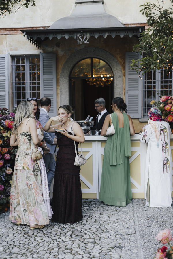 Guests in summer dresses gather at the flower-decorated garden bar.