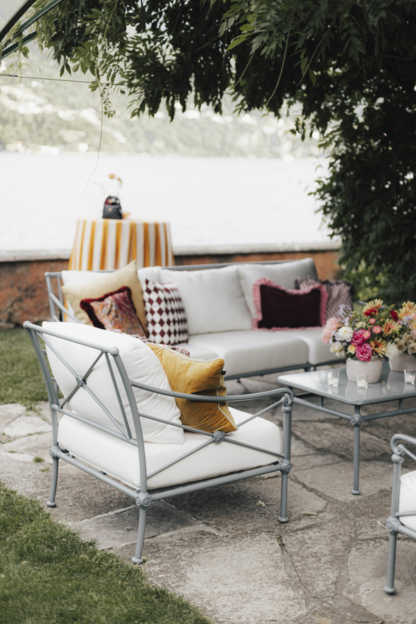 A lakeside lounge with white seating, colourful cushions and flowers at Villa Regina Teodolinda.