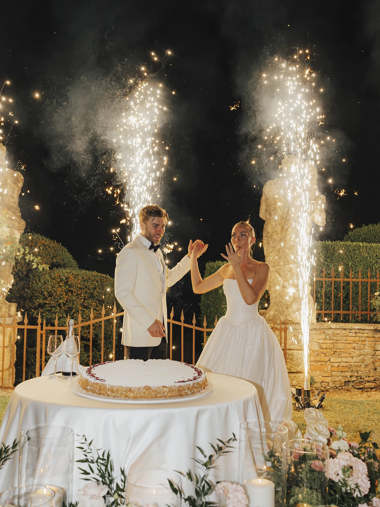 The couple cutting their cake between sparkling fountains