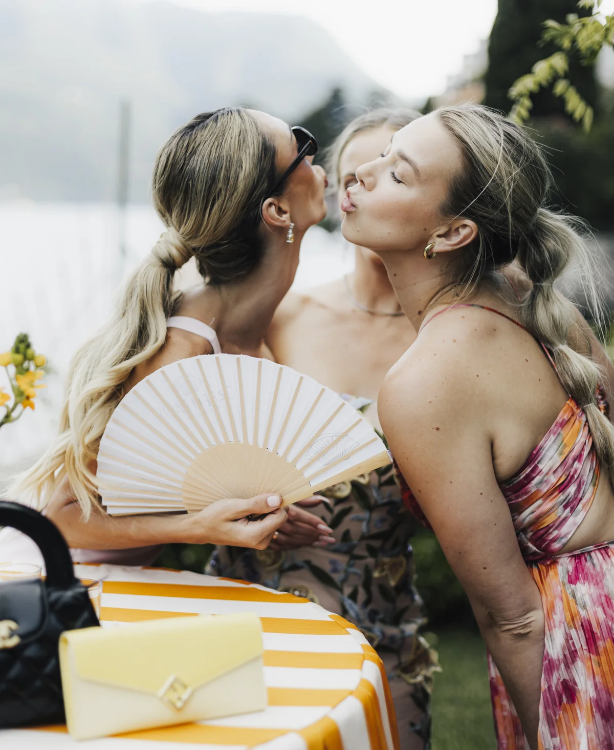 Two wedding guests sharing a kiss with a fan between them