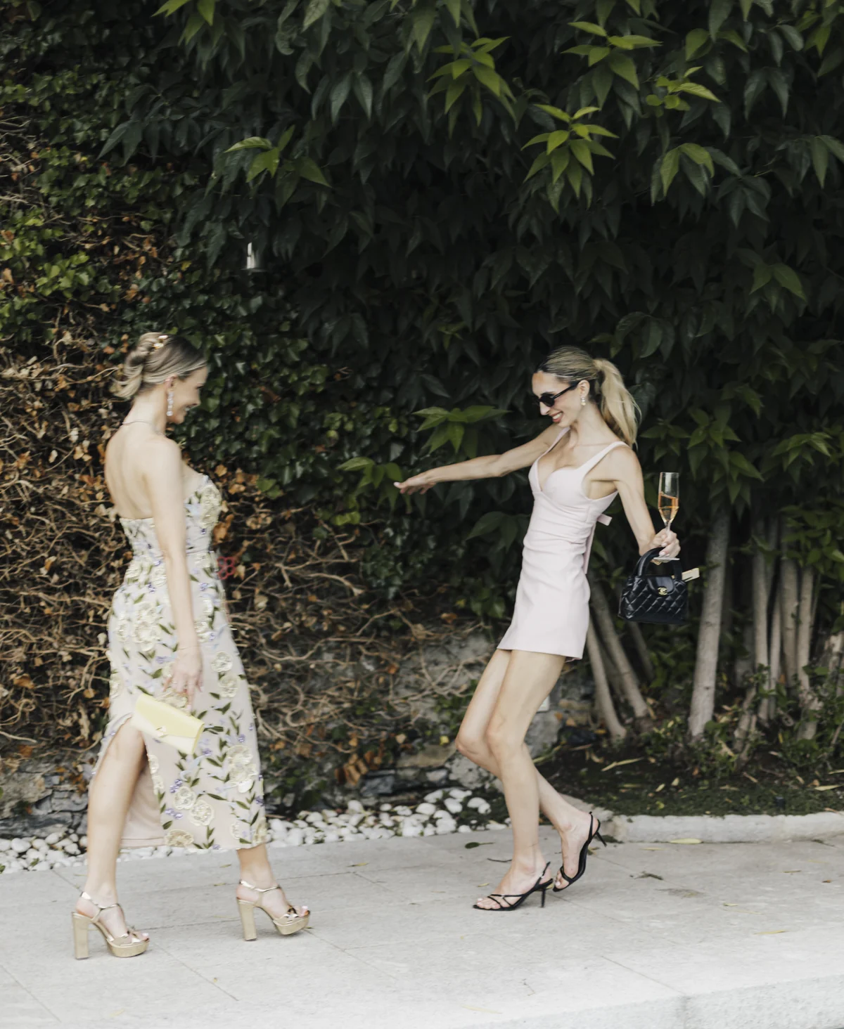 Two fashionably dressed guests meeting beside a garden pool