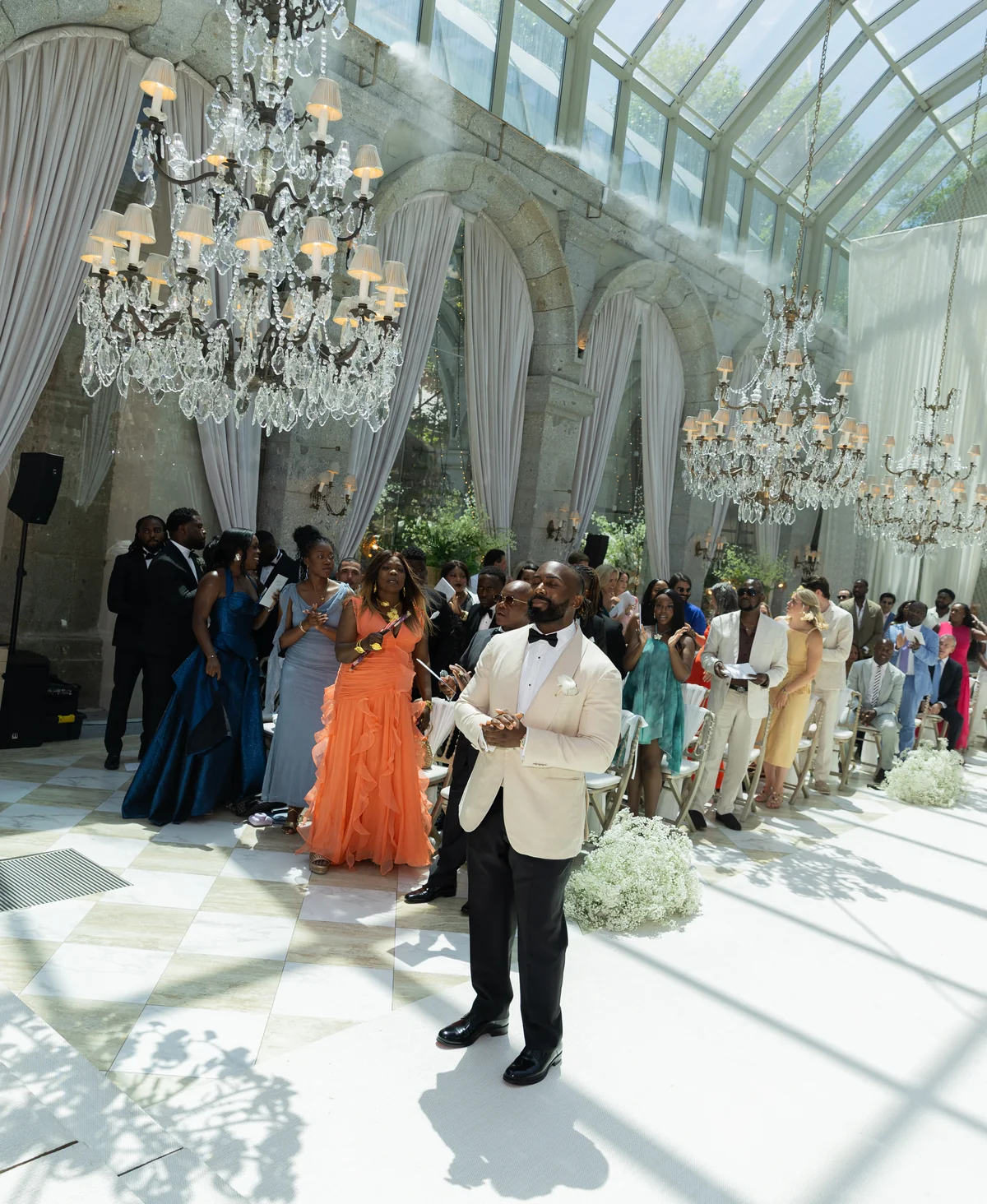 Wedding guests in colourful formalwear beneath crystal chandeliers