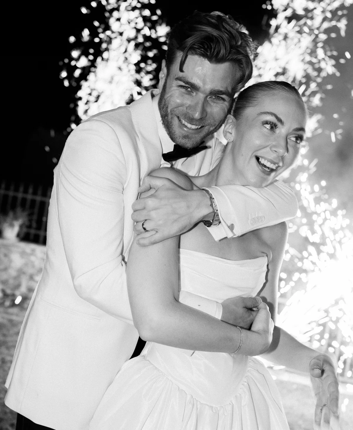 Newlyweds laughing together beneath fireworks in black and white
