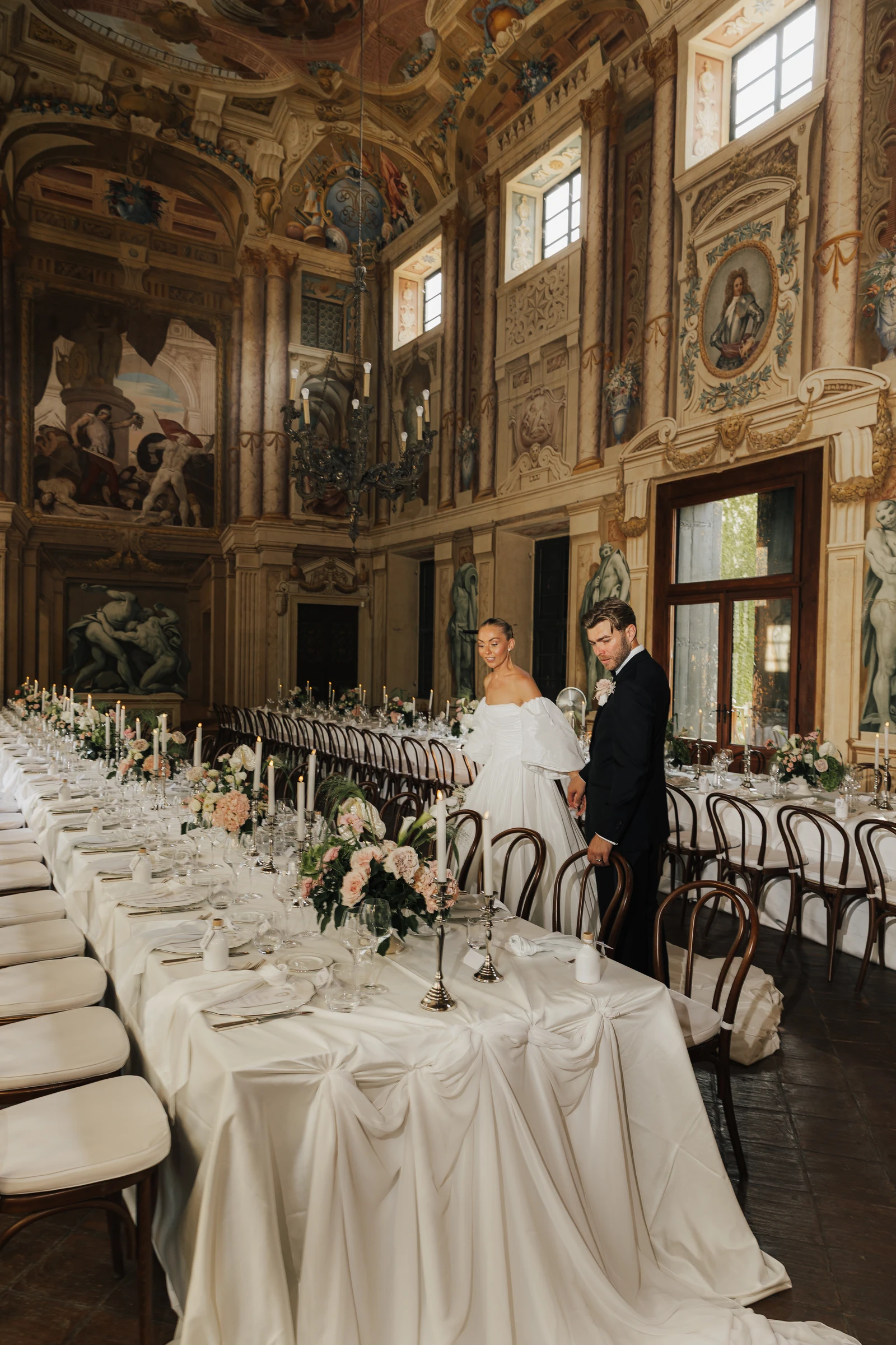 Newlyweds beside a candlelit reception table in the frescoed hall at Villa Arvedi.