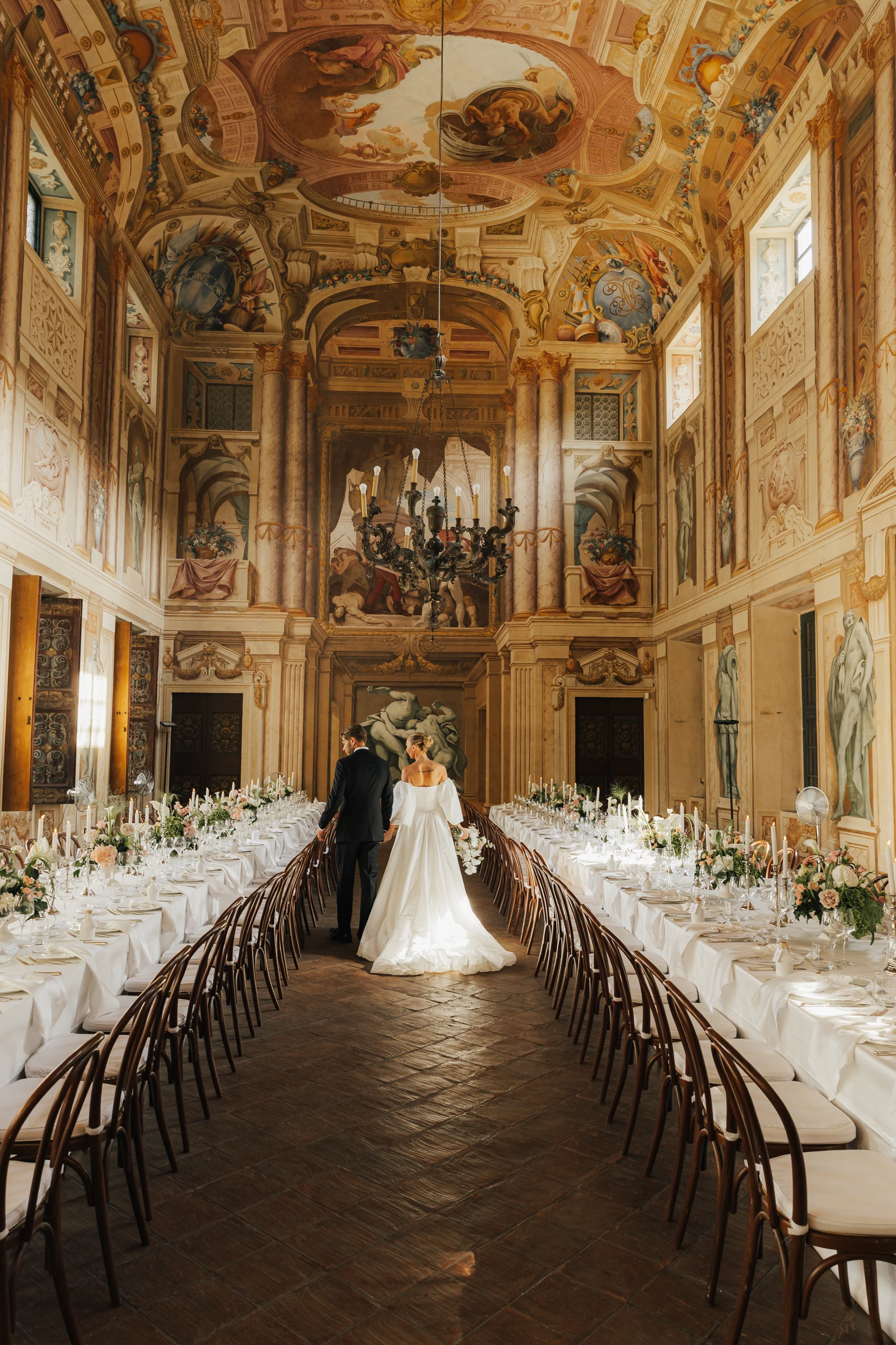 Newlyweds between the dinner tables in the frescoed hall at Villa Arvedi near Verona.