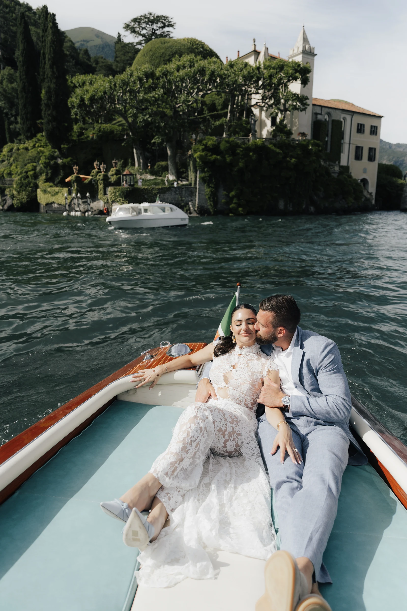 Couple smiling together on a boat with Villa del Balbianello behind them on Lake Como.